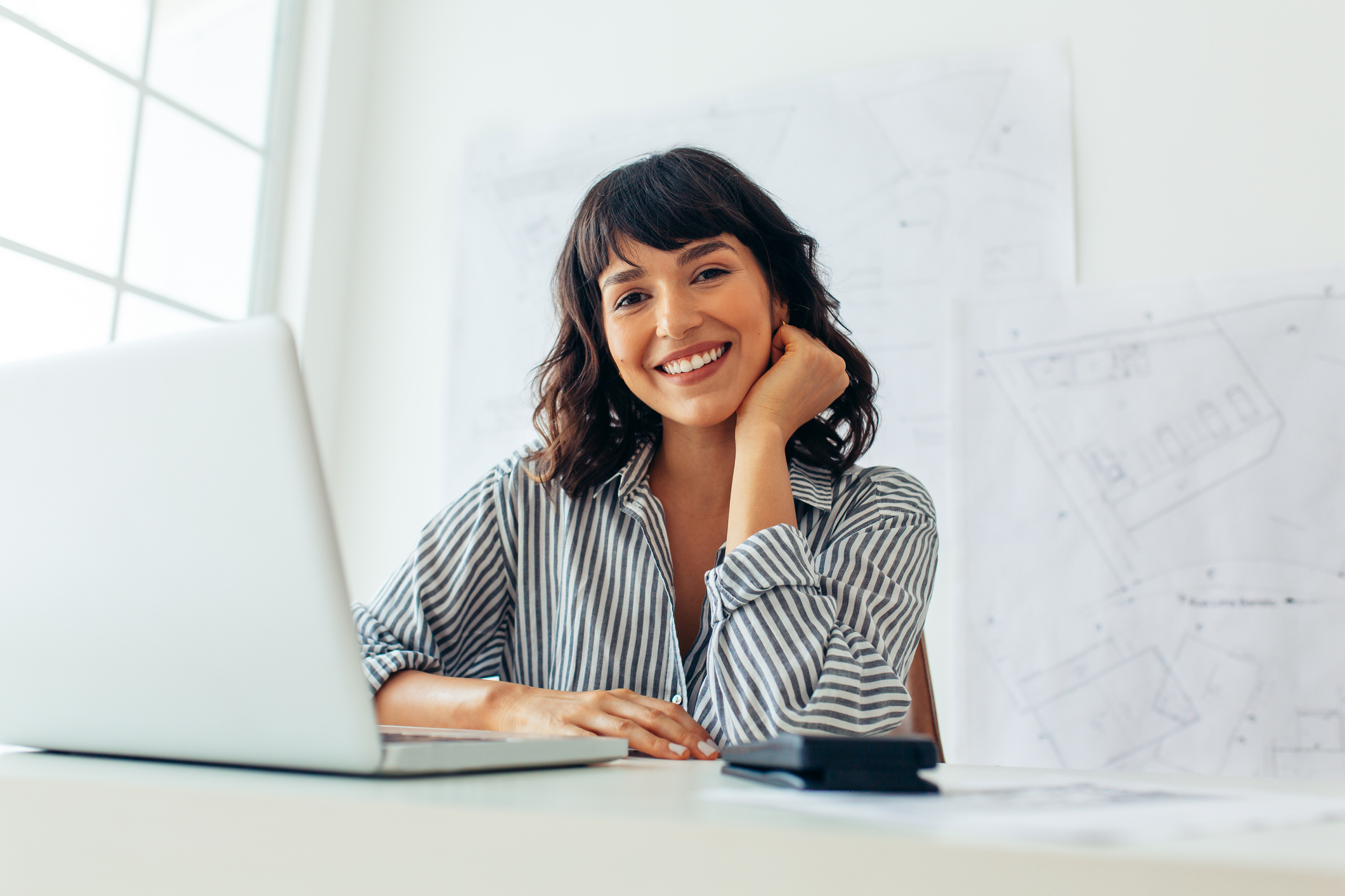 Businesswoman sitting at her desk working on laptop smiling.