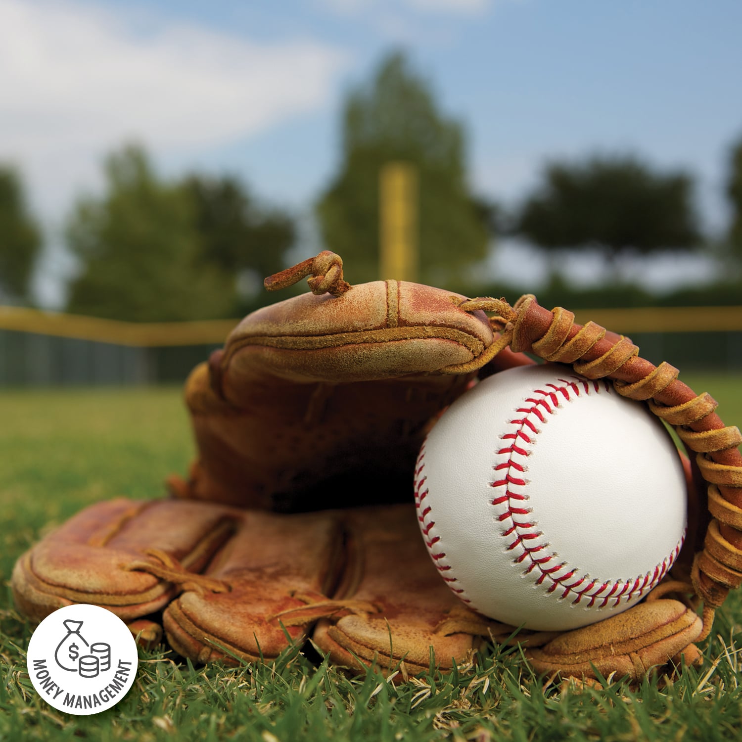 A baseball is inside of a baseball glove, which is laying on green grass, in the background you can see the outfield fence.