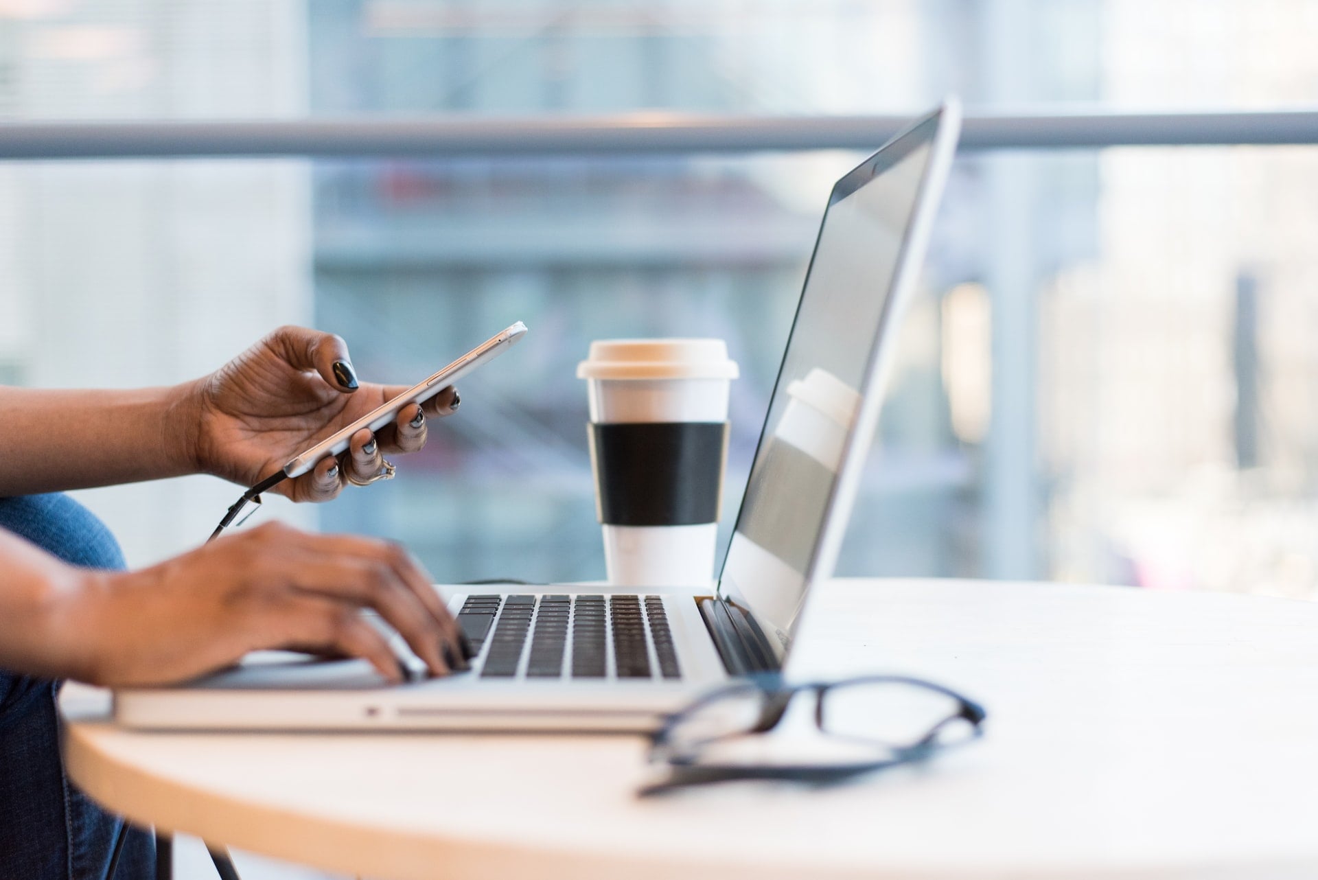 Side image of a person working on a laptop with one hand and a cell phone in the other.