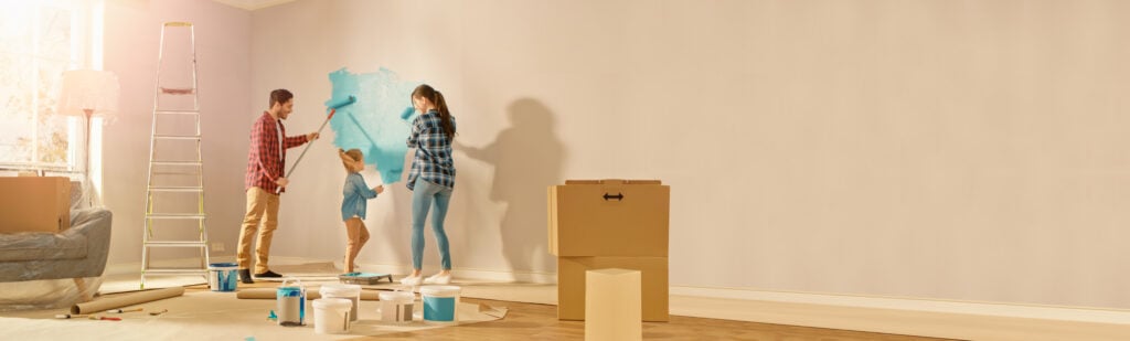 A couple and their child are painting a living room wall with a roller brush.