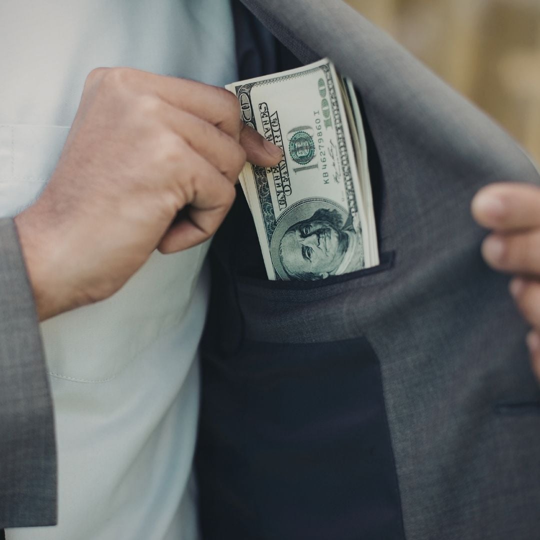 A man slides a small stack of one-hundred-dollar bills into the inside pocket of his suit jacket.