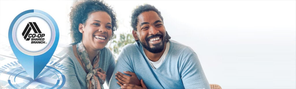 A smiling couple sit on a couch.