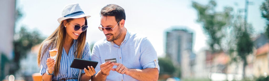A couple sitting outside, shopping on a tablet with credit card in hand.