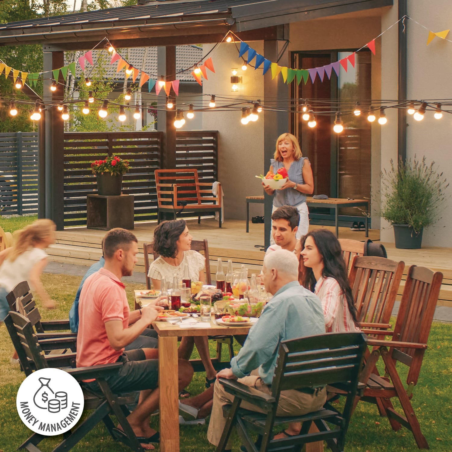 A group of family and friends gather around a table in a backyard lit up with hanging lights