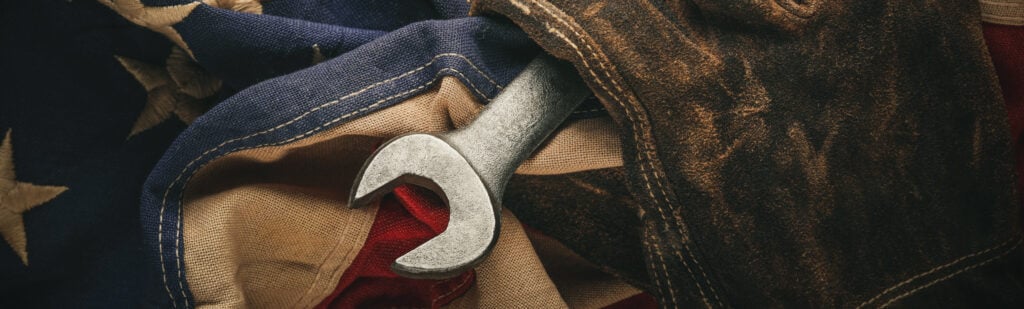 A leather work glove holds a wrench with an American flag in the background