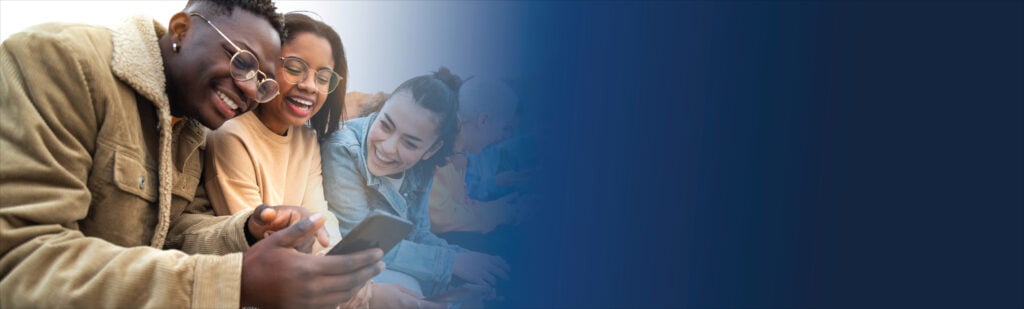 A group of young people smile while gathered around a cell phone.