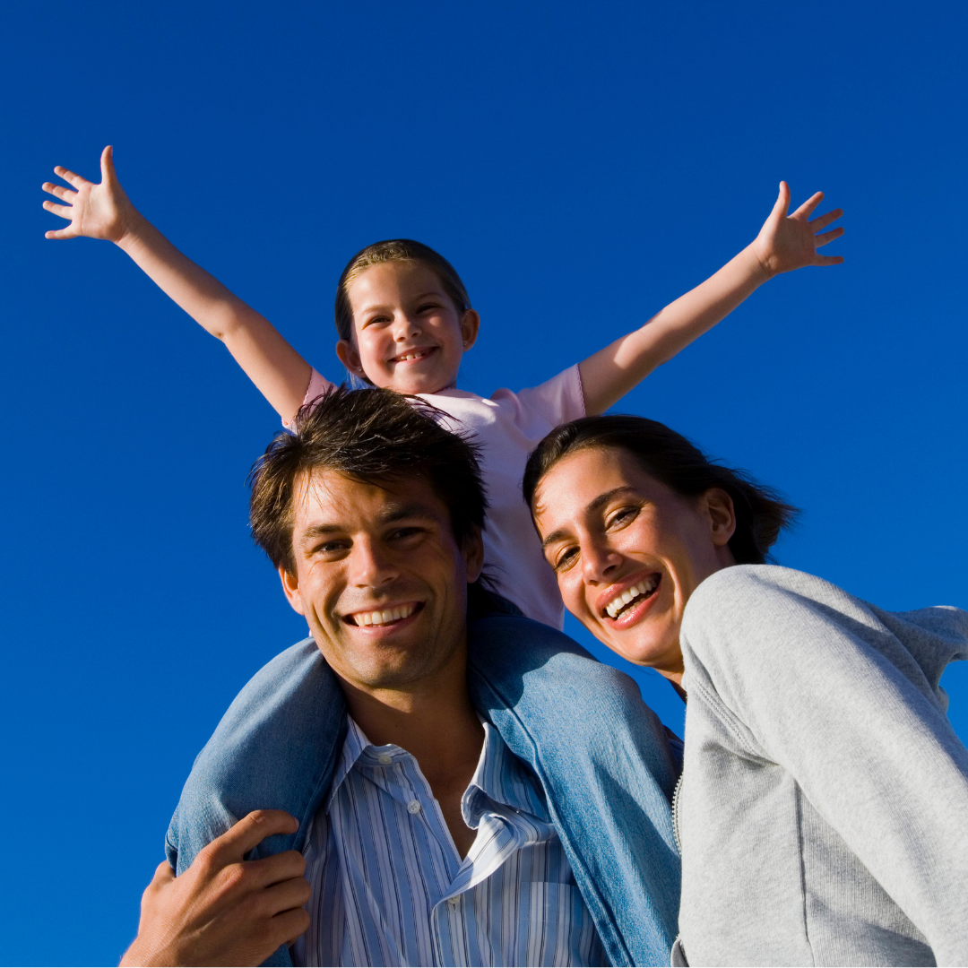 The camera angle points up towards a couple with a young daughter on the father's shoulders with a blue sky in the background.